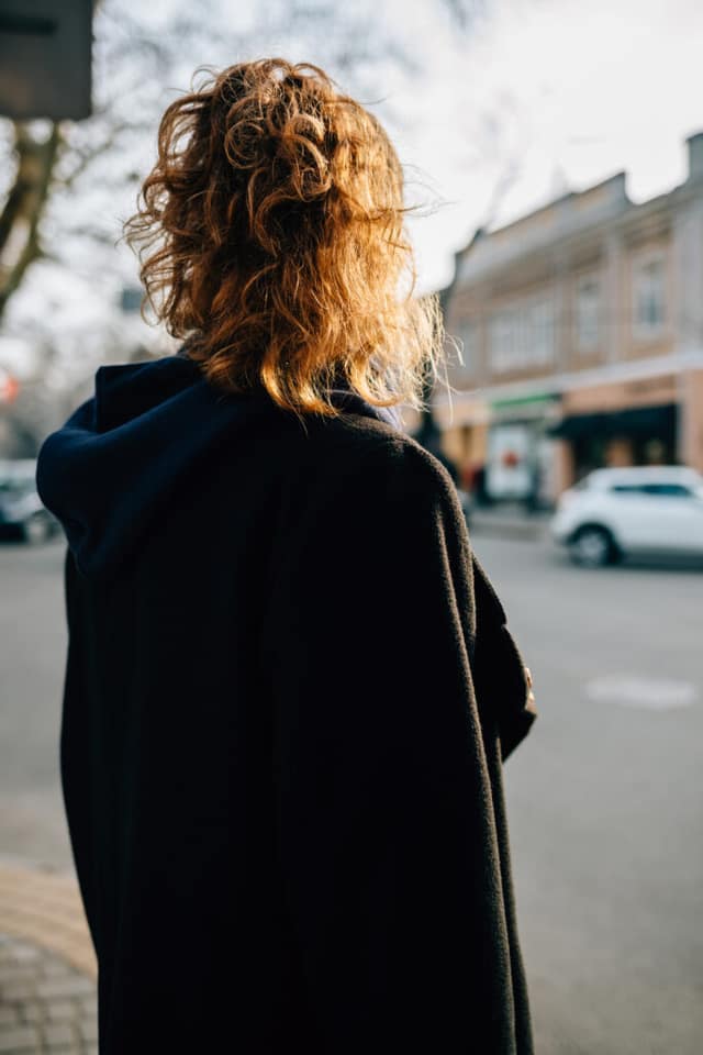 An unknown young person on the road, warmly dressed in a green hood and black jacket. The image is used for PolicyWise for Children & Families' report that research points to childhood roots of youth homelessness.
